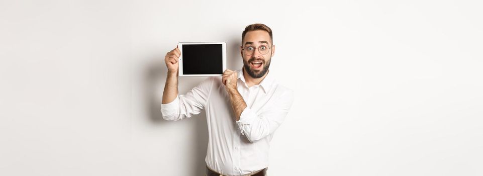 Shopping and technology. Handsome man showing digital tablet screen, wearing glasses with white collar shirt, studio background.
