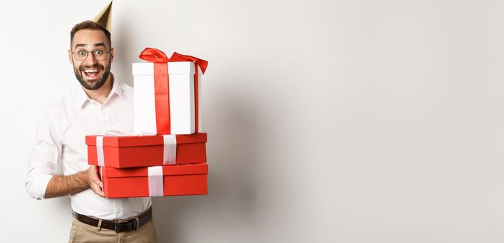 Holidays and celebration. Happy man receiving gifts on birthday, holding presents and looking excited, standing over white background.