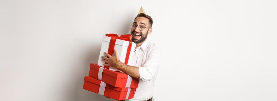 Holidays and celebration. Excited man having birthday party and receiving gifts, looking happy, standing over white background.