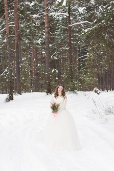 Beautiful bride in a white dress with a bouquet in a snow-covered winter forest. Portrait of the bride in nature.