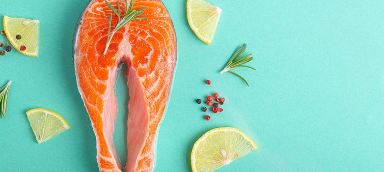 Uncooked raw fresh fish salmon steak top view on blue background with rosemary, lemon wedges and spices, delicacy healthy fish cooking and nutrition concept flat lay copy space