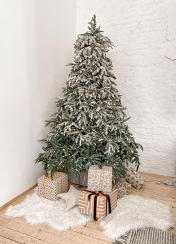 Christmas decorated fir tree with garland and fake snow in gray, white, silver colours with gifts on rustic wooden parquet floor with fur carpets next to white brick wall. Christmas morning.