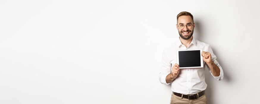 Shopping and technology. Handsome man showing digital tablet screen, wearing glasses with white collar shirt, studio background.