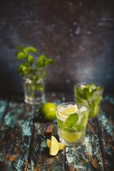 Summer drink Mojito with ice, brown sugar, lime slices, fresh mint in glass, wooden rustic background, angle view. Cold refreshing cocktail great for summer party and fun