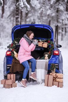 A woman in winter clothes drinks a hot drink sitting in a car decorated in a New Year's way. Traveling by car through the forest. A trip before Christmas.