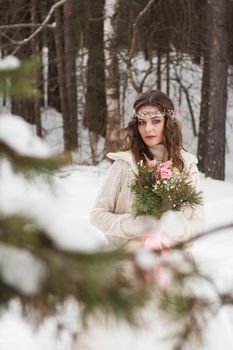 Beautiful bride in a white dress with a bouquet in a snow-covered winter forest. Portrait of the bride in nature.