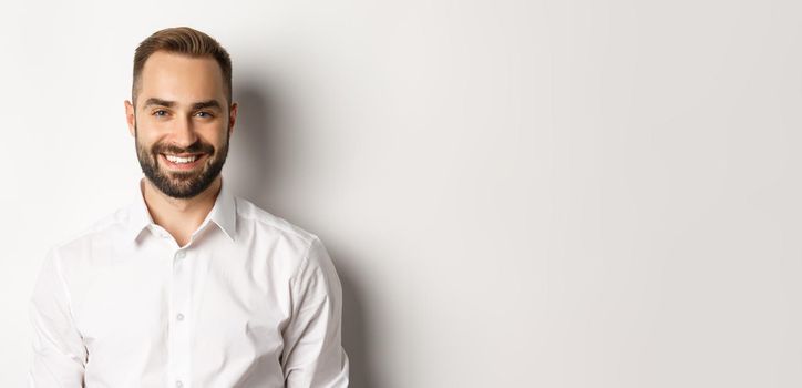 Close-up of confident male employee in white collar shirt smiling at camera, standing self-assured against studio background.