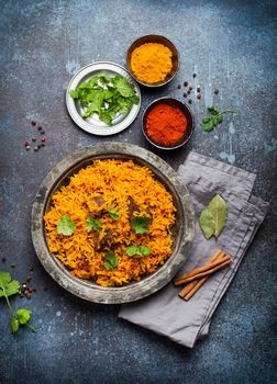 Pilaf - traditional Eastern/Asian dish made with rice, vegetables and meat served on vintage plate with fresh cilantro, sauces and spices on rustic background, top view, close-up