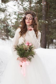 Beautiful bride in a white dress with a bouquet in a snow-covered winter forest. Portrait of the bride in nature.