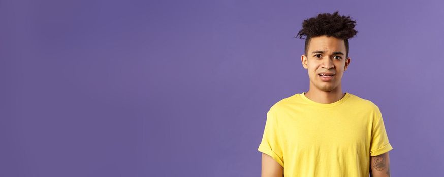 Waist-up portrait of young concerned hispanic man with worried gaze looking at camera, frowning being scared for friend stuck in troublesome situation, want help, stand purple background.