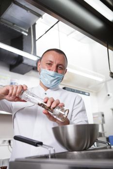 Vertical portrait of a chef in medical face mask salting prepared meal at restaurant kitchen