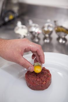 Vertical close up of a chefs hand putting quail egg on tartar dish