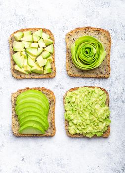 Concept of healthy breakfast toasts with avocado smashed, slices, chunks and rose. Different ways of making and serving delicious avocado sandwich, top view, white stone background, close-up