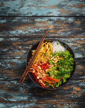 Asian, Chinese or Vietnamese style noodles salad with fresh vegetables, fried tofu and peanuts, served in rustic ceramic bowl on colorful wooden background. Healthy diet clean eating or vegan concept