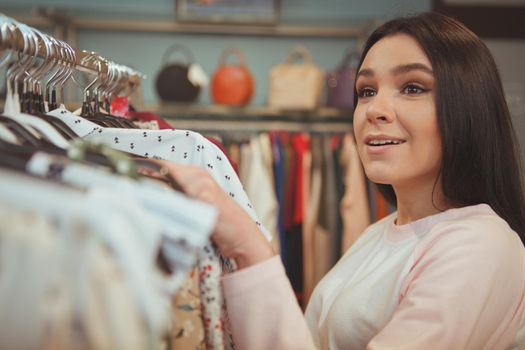 Cropped shot of a young beautiful woman looking overwhelmed, while choosing new clothes to buy. Attractive female customer examining clothes on sale at fashion store, copy space