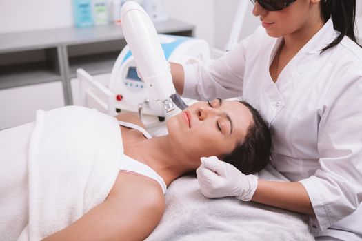 Young woman getting facial hair removed by professional cosmetologist. Cropped shot of a beautician using laser hair removal machine on a female client
