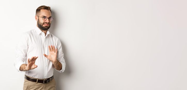 Disgusted businessman rejecting something bad, cringe from aversion, showing stop sign, standing over white background.