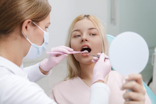 Woman looking into mirror while dentist checking her teeth