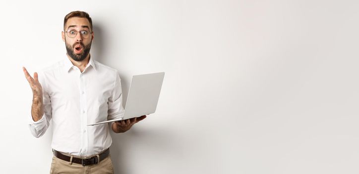 Business. Man holding laptop and looking amazed, surprised with website, standing over white background. Copy space