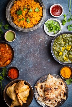 Overhead of Indian traditional dishes and appetizers: chicken curry, pilaf, naan bread, samosas, paneer, chutney on rustic background. Table with choice of food of Indian cuisine, space for text