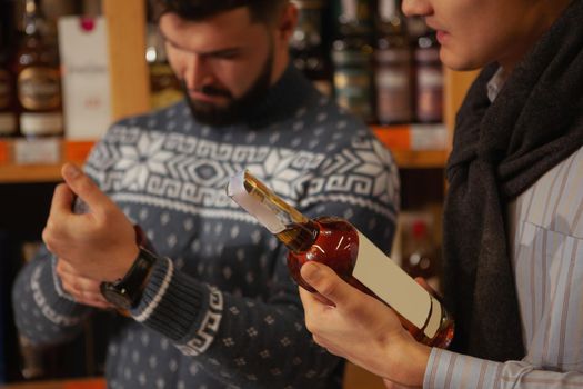 Cropped shot of two men examining alcohol on sale at the supermarket. Male friends preparing for a party, choosing wine to buy