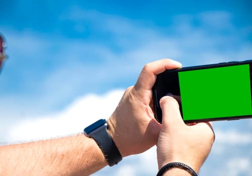 Hand holding smartphone on sky background. template for design. mockup selfie green background. blank advertising smartphone display. Modern black phone in man hand. white screen mockup