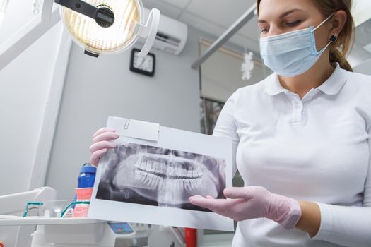 Female dentist wearing medical face mask showing dental x-ray to the camera