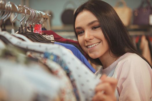 Cropped close up of a beautiful cheerful woman smiling, examining clothing on sale. Happy female customer enjoying seasonal discount, while shopping at clothes store, copy space