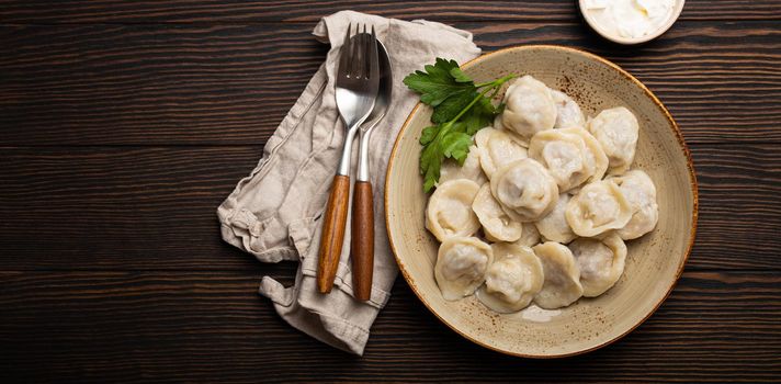 Pelmeni, traditional dish of Russian cuisine, boiled dumplings with minced meat filling on plate with sour cream sauce on wooden rustic background table from above food composition space for text