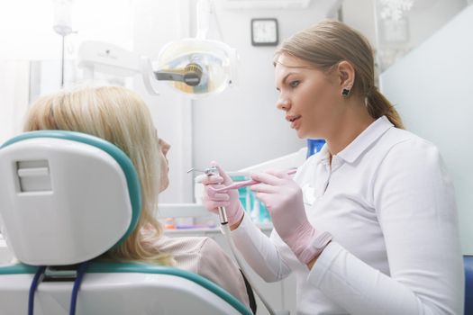 Young female dentist working at her clinic, talking to her patient