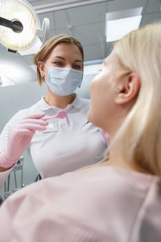 Vertical shot of a female professional dentist in medical face mask working at her dental clinic