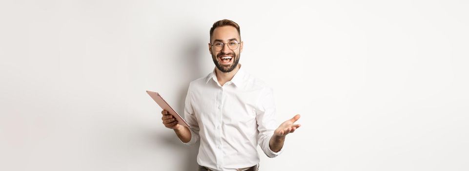 Satisfied businessman praising good work, reading report on digital tablet, standing happy against white background.