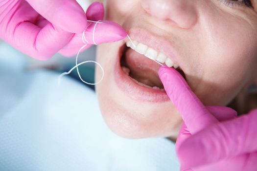 Cropped close up of a dentist using dental floss, cleaning teeth of patient
