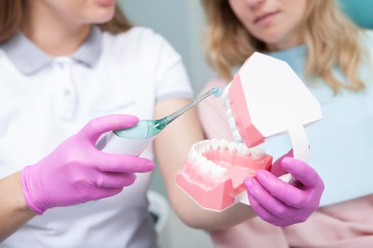 Selective focus on ultrasonic toothbrush and jaw model in hands of female dentist