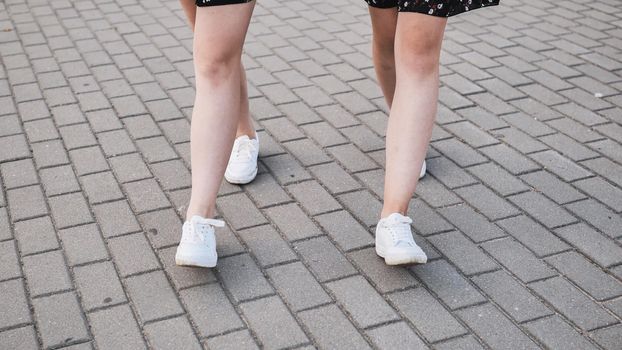 Two friends in white sneakers walk down the street