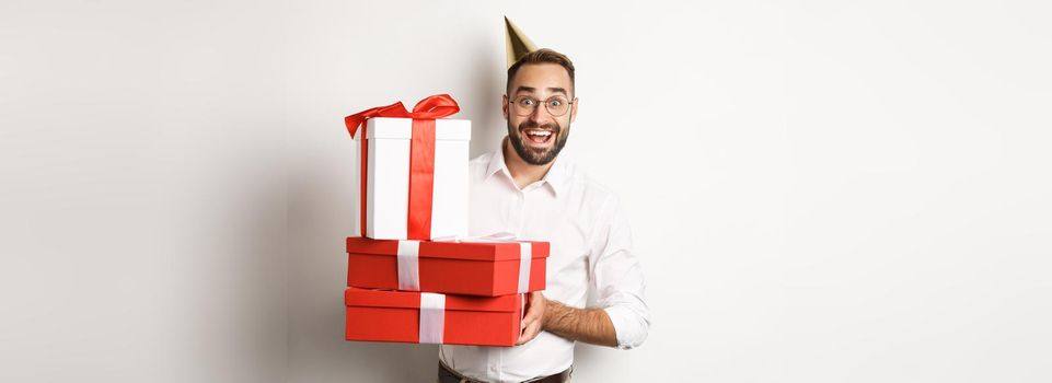 Holidays and celebration. Happy man receiving gifts on birthday, holding presents and looking excited, standing over white background.