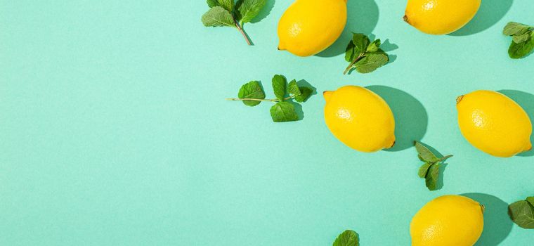 Fresh yellow lemons with mint on minimal blue background on bright sun light with hard shadows pattern summer background flat lay from above, citrus food composition, space for text