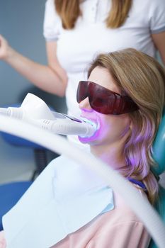 Vertical shot of a woman wearing protective eyeglasses during dental whitening treatment