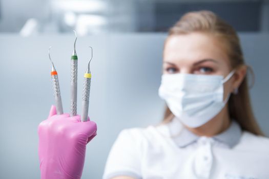 Selective focus on dental tools in the hand of female dentist wearing medical face mask