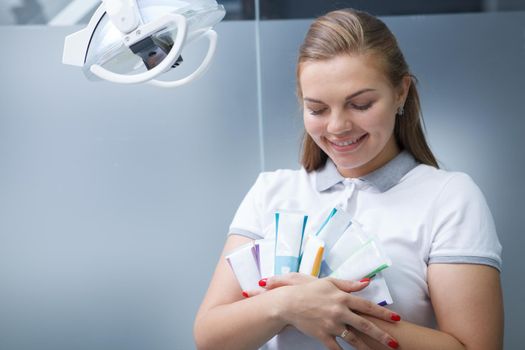Lovely young female dentist hugging many toothpaste tubes, smiling joyfully, copy space