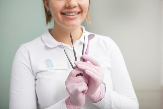 Cropped shot of a female dentist with braces smiling, holding dental tools