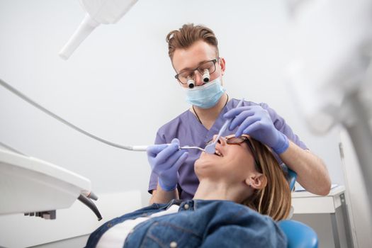 Low angle shot of a dentist wearing microscope glasses, examining teeth of patient, copy space