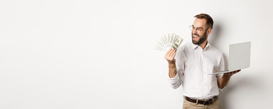 Business and e-commerce. Successful businessman using laptop for work and holding money, standing over white background.