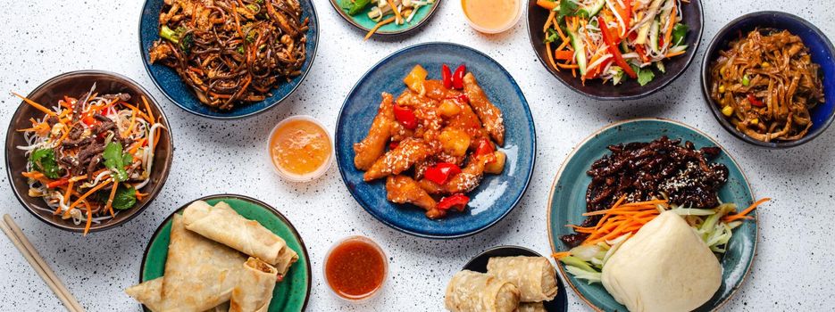 Set of Chinese dishes on white table: sweet and sour chicken, fried spring rolls, noodles, rice, steamed buns with bbq glazed pork, Asian style banquet or buffet, top view .