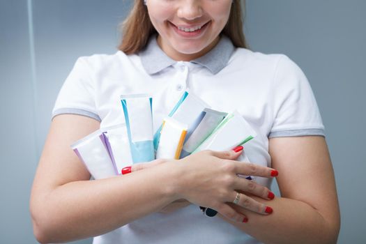 Unrecognizable female dentist smiling, carrying bunch of toothpaste tubes