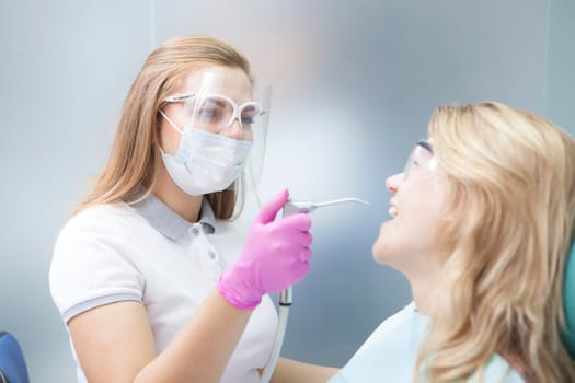 Female dentist wearing medical face mask and plastic face shield, working with female patient during coronavirus pandemic