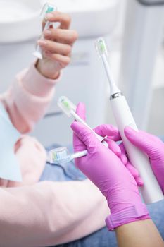 Vertical cropped shot of a dentist showing to her patient electric toothbrush with various replacement heads