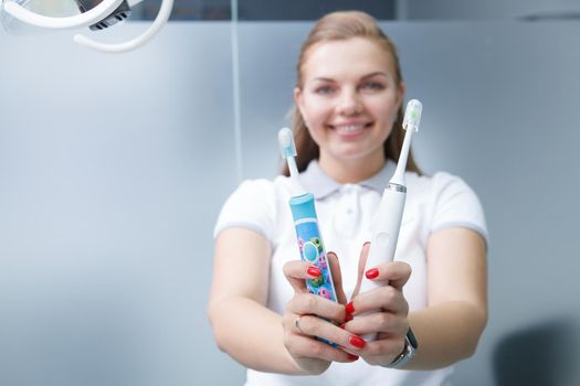 Selective focus on electric toothbrushes happy female dentist is holding out to the camera