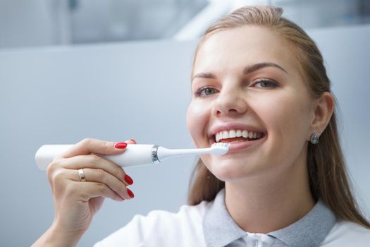 Close up of a charming young female dentist smiling, using electric toothbrush on her teeth