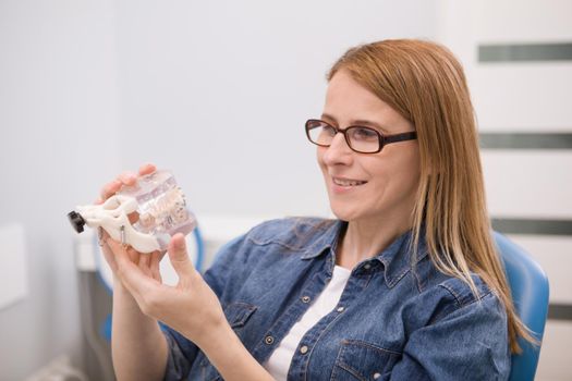 Mature woman looking at dental mold with braces, sitting in dental chair